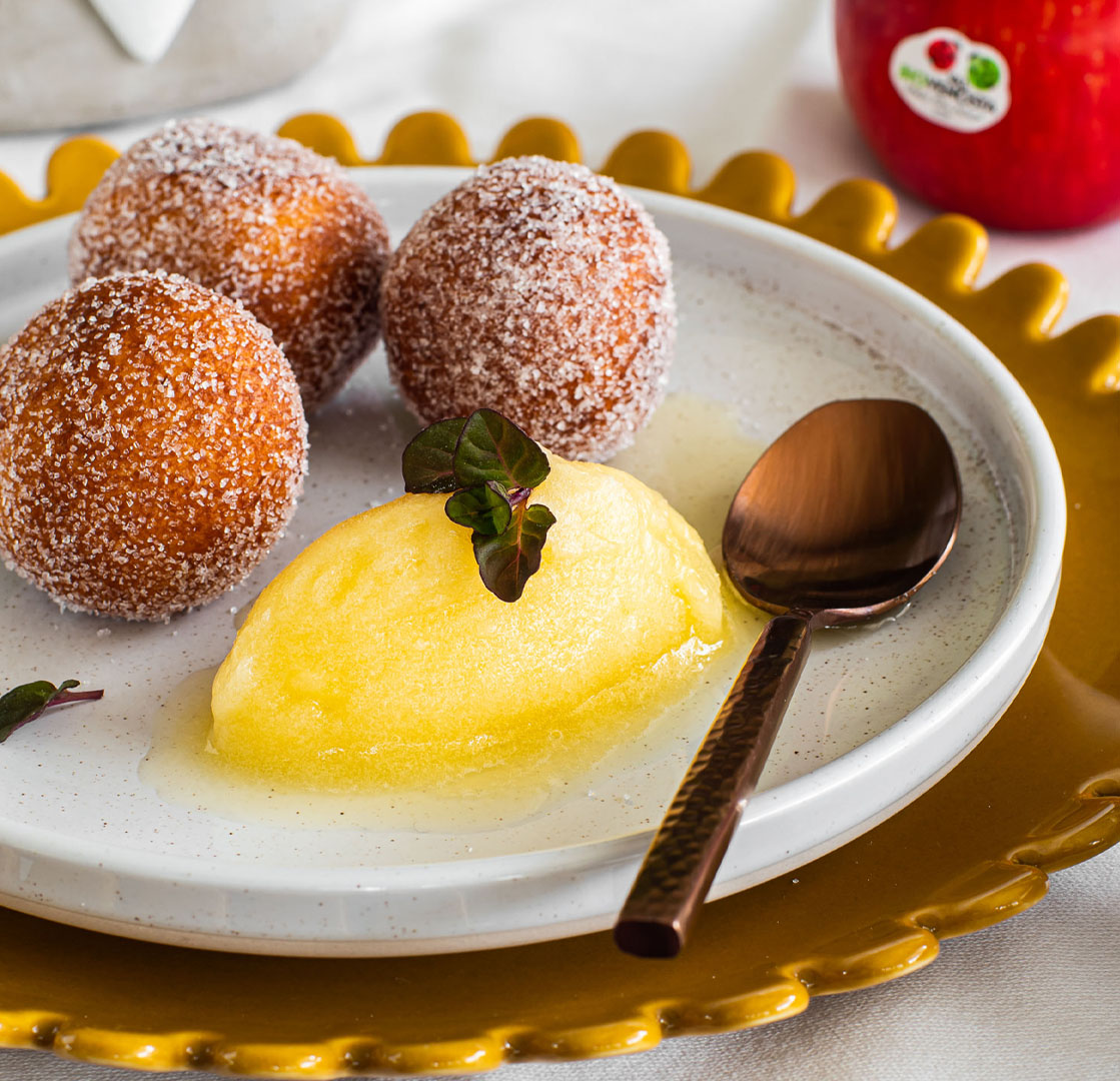 Piatto con canederli di ricotta fritti e sorbetto alle mele Topaz Bio, decorato con foglie verdi e servito accanto a una mela rossa e un fiore giallo.