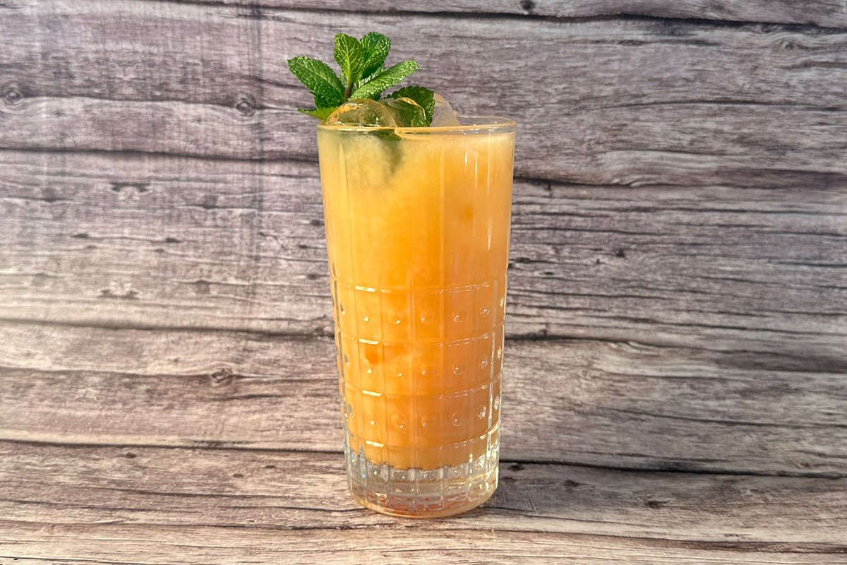 Un bicchiere tumbler alto con bevanda analcolica all'arancia guarnito con rametto di foglie di menta fresca.