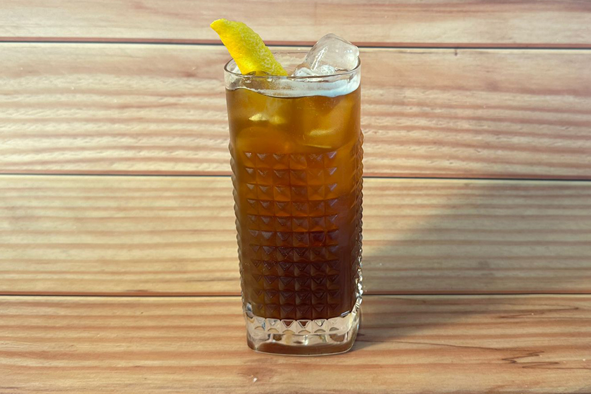 Un mocktail tropicale servito in un bicchiere alto, con ghiaccio e decorato con zest di limone.