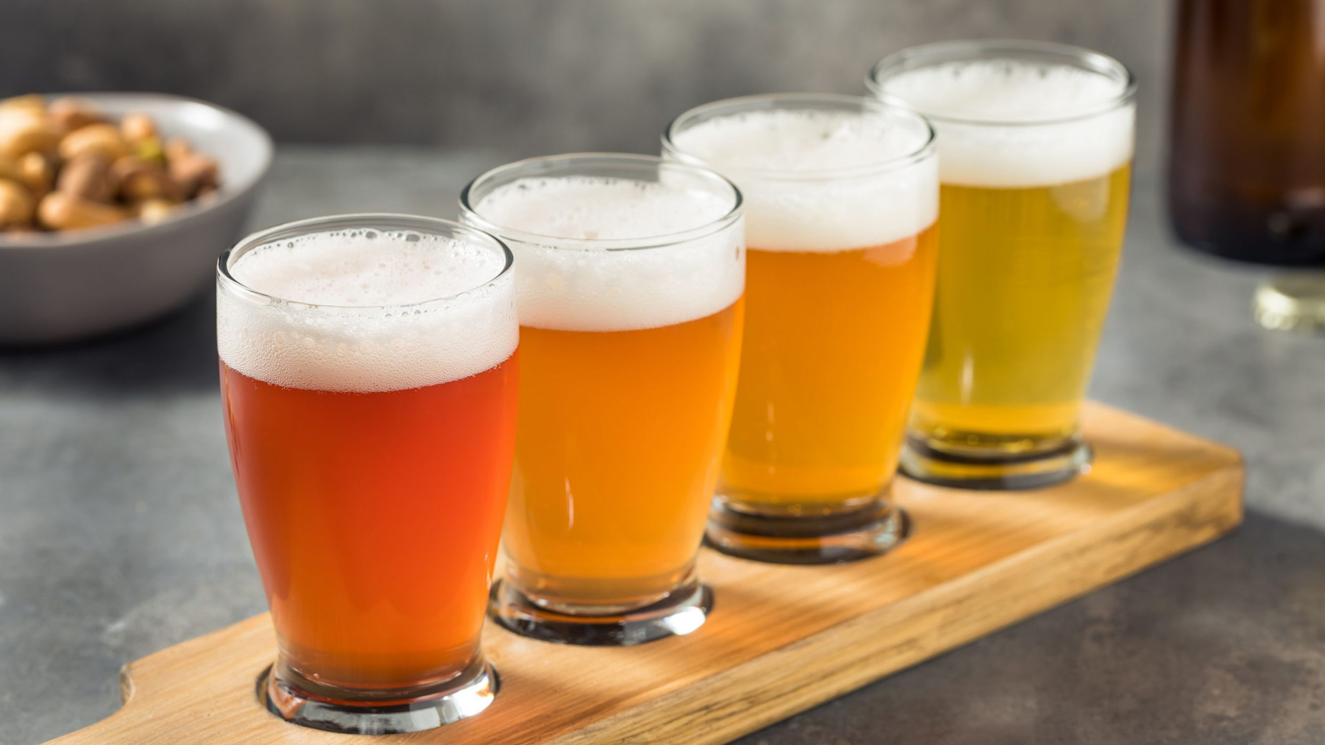 Quattro bicchieri di birra artigianale. tutte le birre ad alta fermentazione disposte su un vassoio di legno, con colori che variano dal dorato al rame intenso, schiuma densa e sfondo sfocato con snack.