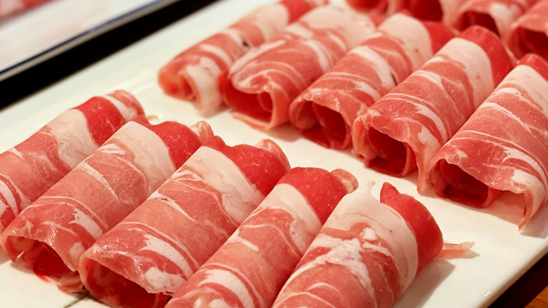 Vassoio con fette di salumi arrotolati, dal colore rosso intenso e venature bianche di grasso, disposti ordinatamente su un piatto bianco per l'evento Distinti Salumi