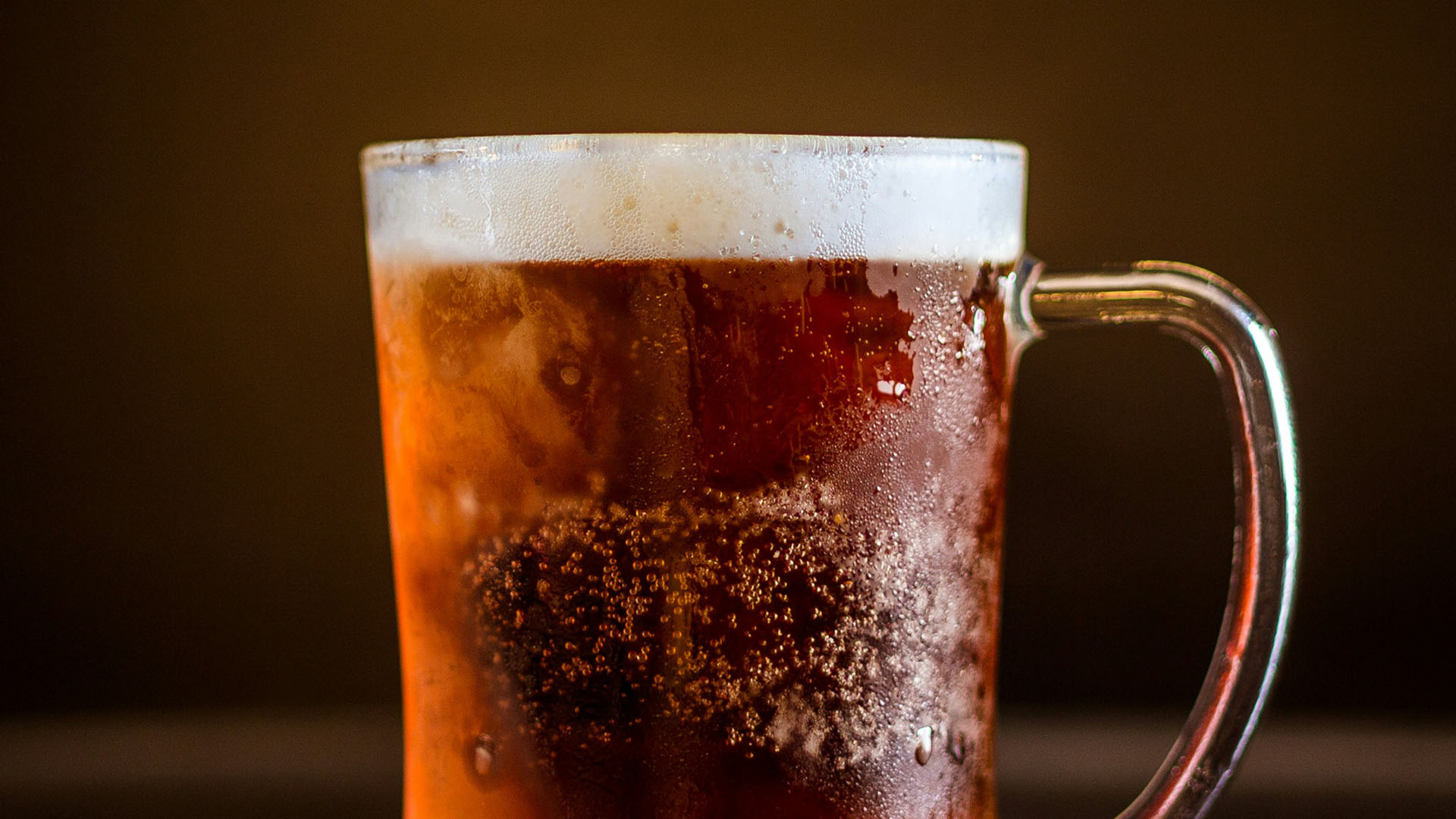 Boccale di birra ambrata con schiuma densa e bollicine visibili, servito freddo con condensa sul vetro, perfetto per una degustazione di birre artigianali. Evento al MOG di Genova con MHOPS