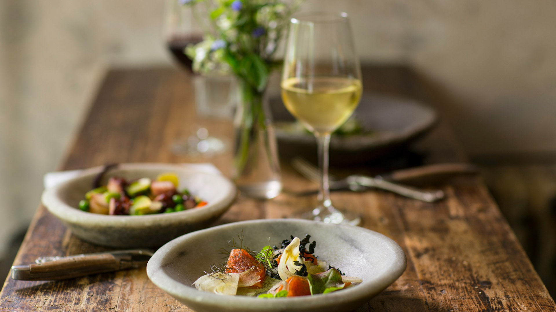Calice di vino bianco su tavola rustica, accompagnato da piatti gourmet. Un perfetto esempio di abbinamenti vino bianco con piatti raffinati e saporiti.
