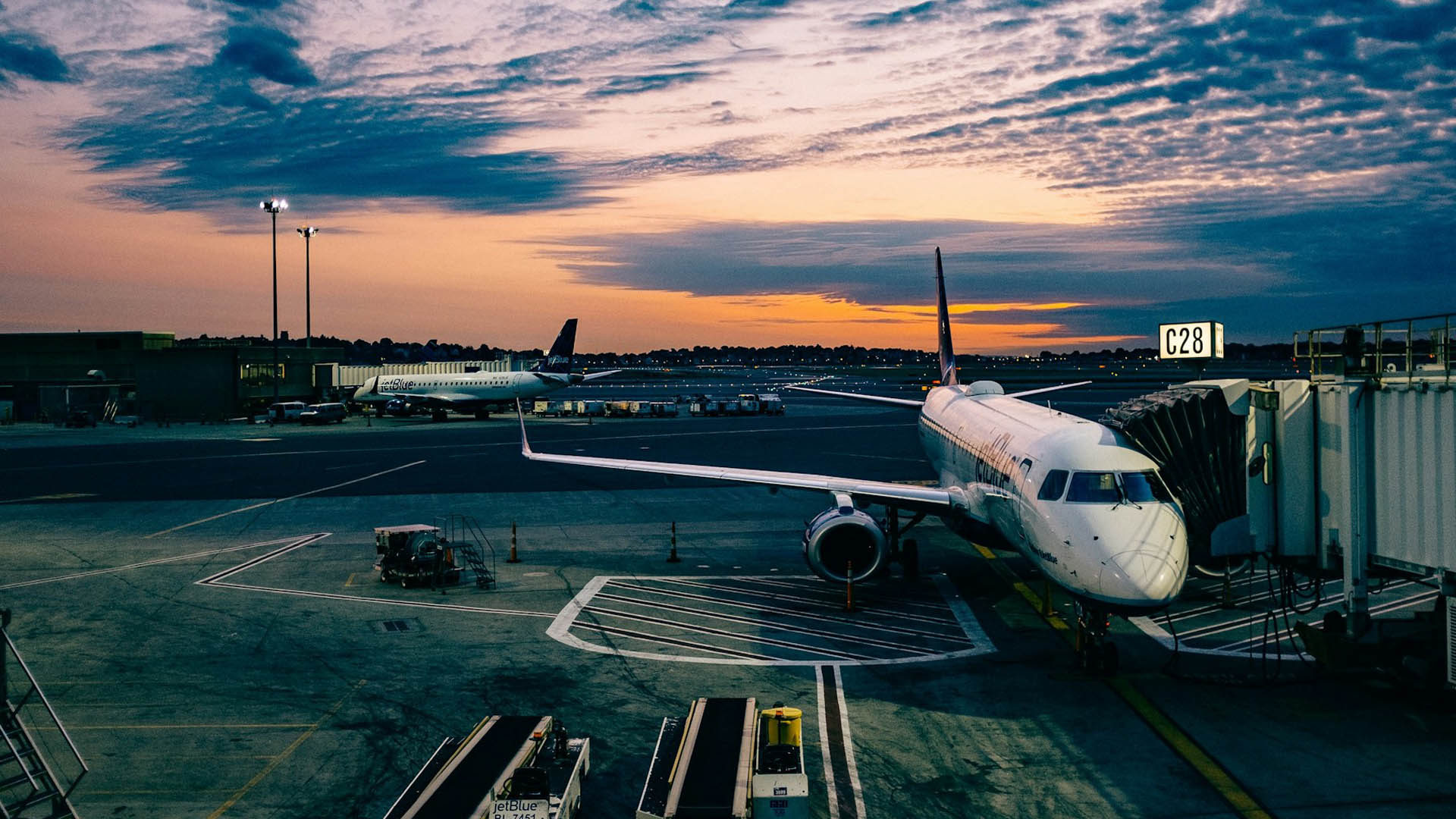 Un aereo pronto al decollo al gate C28 di un aeroporto internazionale al tramonto, con luci accese e cielo dai toni blu e arancio. Meglio non bere birra e alcolici prima del volo