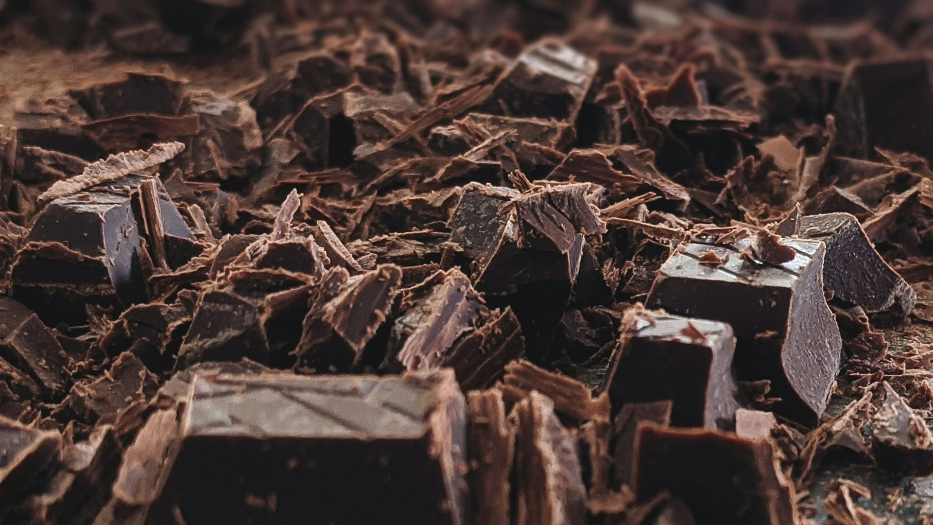 Grosso piano ravvicinato di scaglie e pezzi di cioccolato fondente spezzettato, con texture dettagliata e sfumature intense di marrone scuro. Ritorno a Caserta di Choco Italia 2025