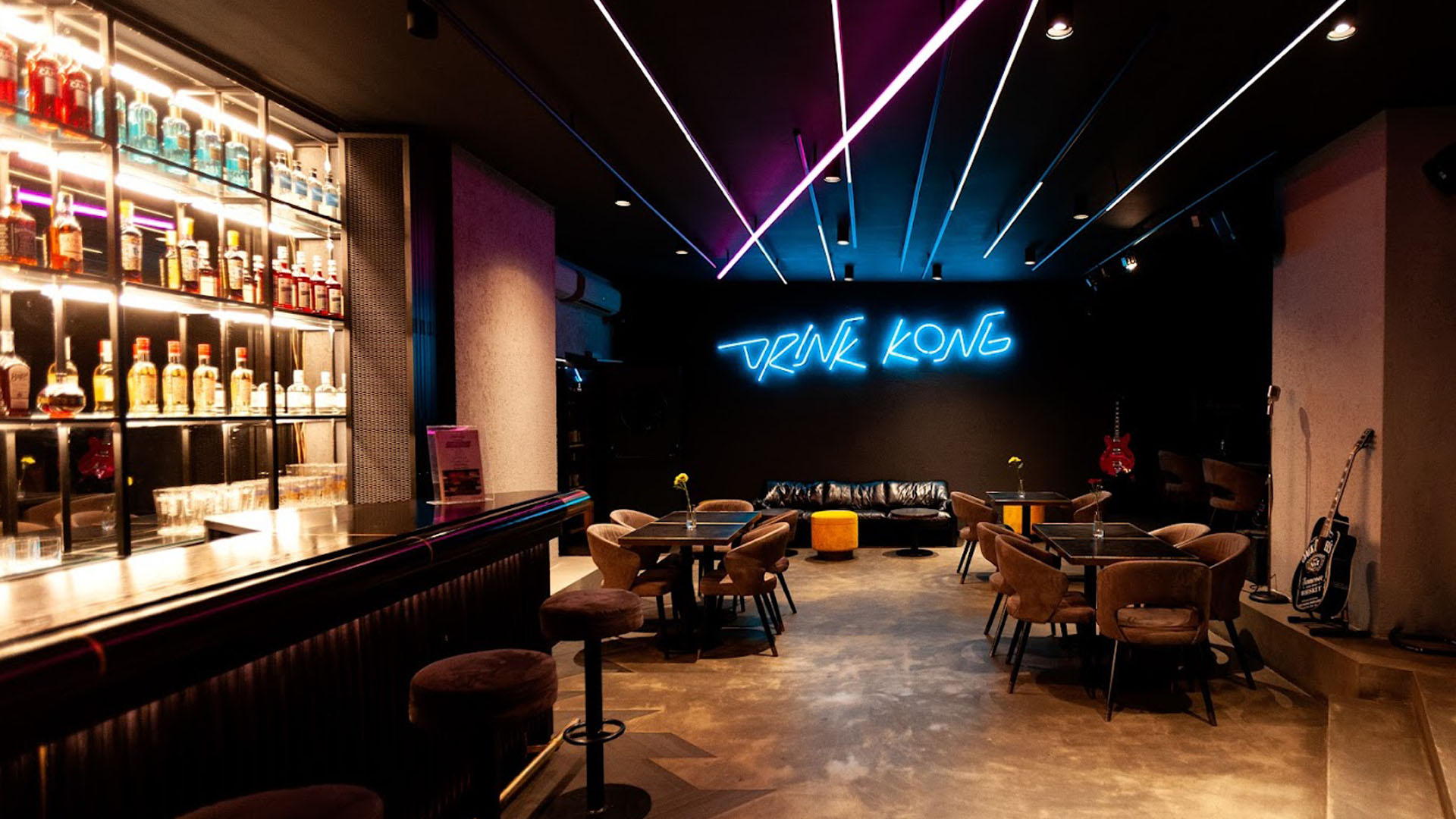 Interno del cocktail bar Drink Kong a Roma, con arredi moderni, luci al neon blu e un'ampia selezione di bottiglie esposte dietro al bancone.