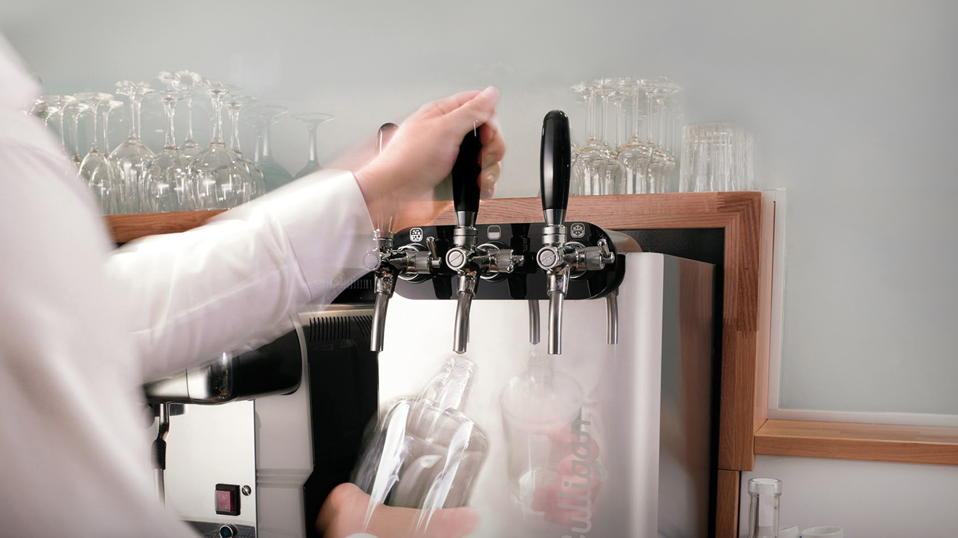 Erogatore professionale Culligan per acqua filtrata con tre rubinetti, in funzione dietro il bancone di un ristorante, mentre un addetto riempie una bottiglia di vetro.