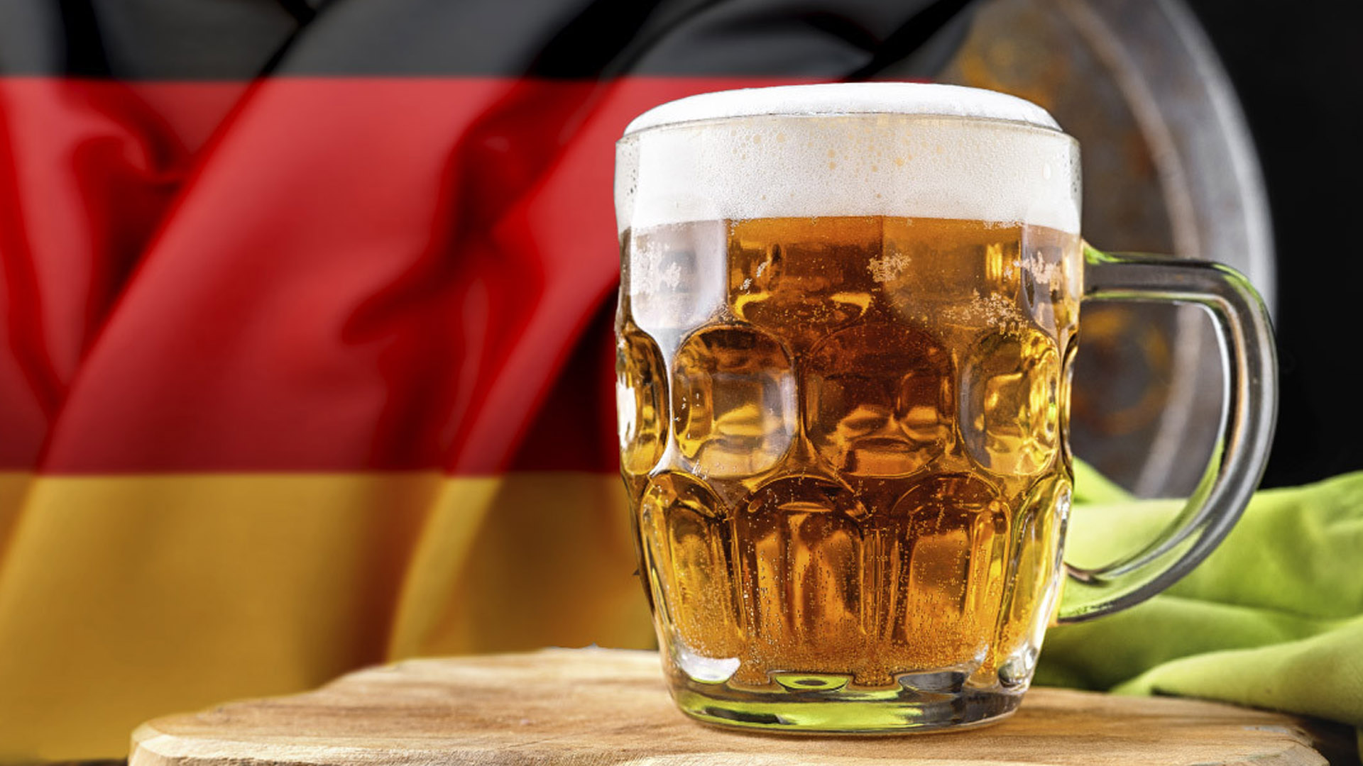 Boccale di birra chiara tedesca con schiuma, davanti a una bandiera della Germania, simbolo dell’editto della purezza e della tradizione birraria tedesca.