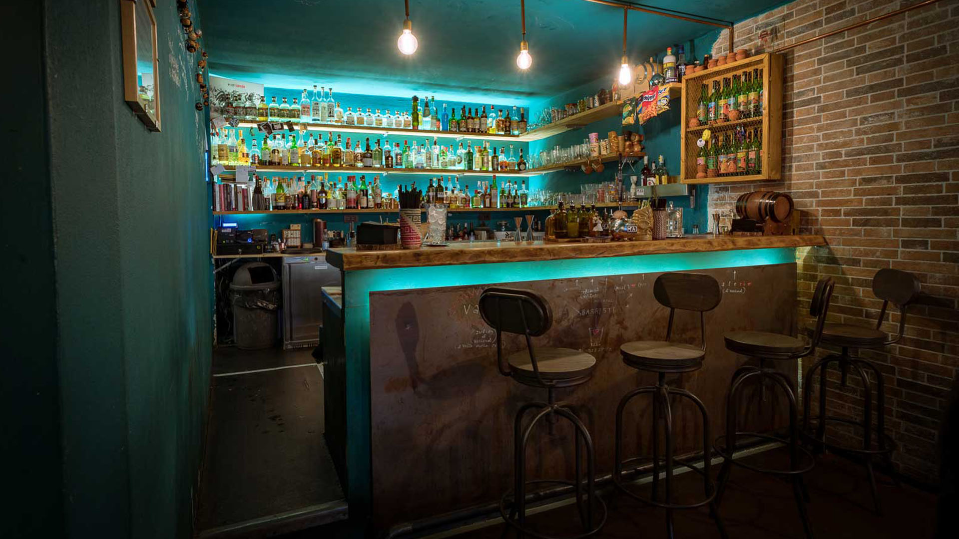 Interno del cocktail bar Mad - Souls & Spirits di Firenze, con bancone in legno illuminato da luci al neon azzurre, bottiglie esposte e sgabelli in metallo.