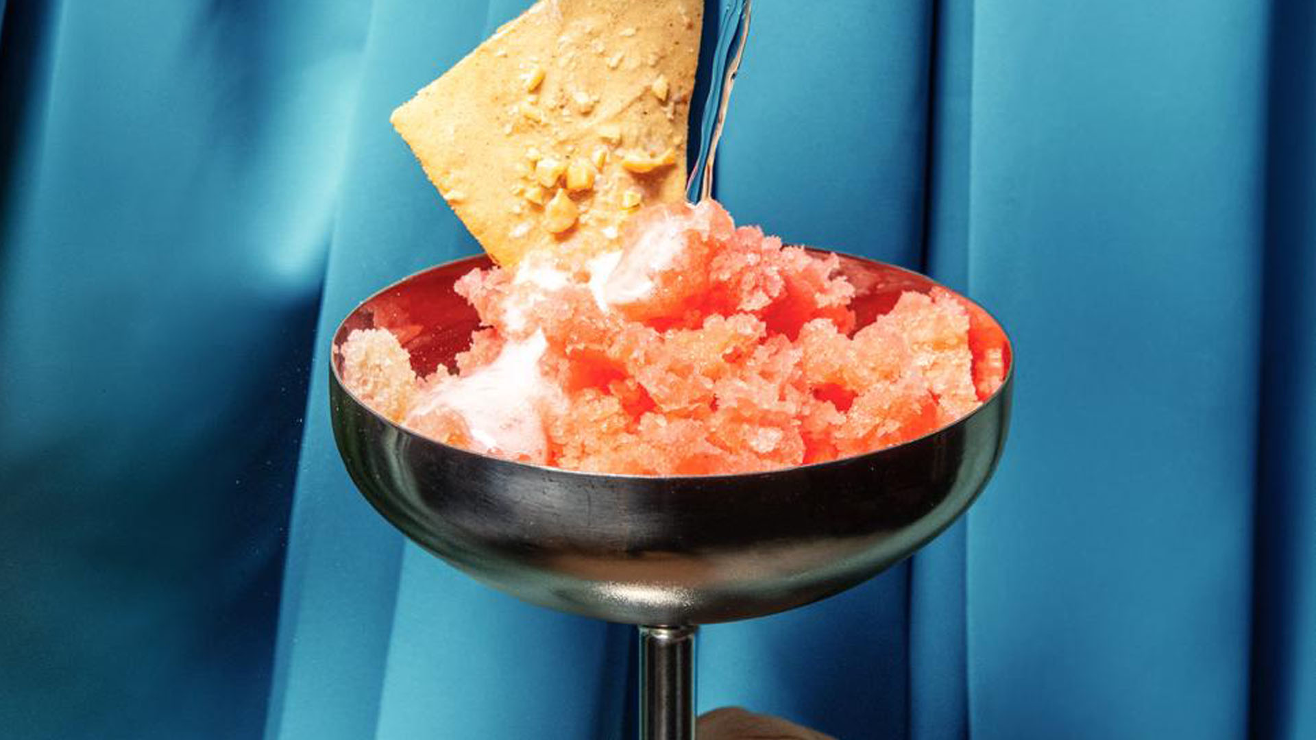 Cocktail estivo del bar Eredi Borgnino con gelato all’Aperol, burro di arachidi e champagne servito in coppa metallica su sfondo blu. Nuova drink list nel cocktail bar bistrot di Torino