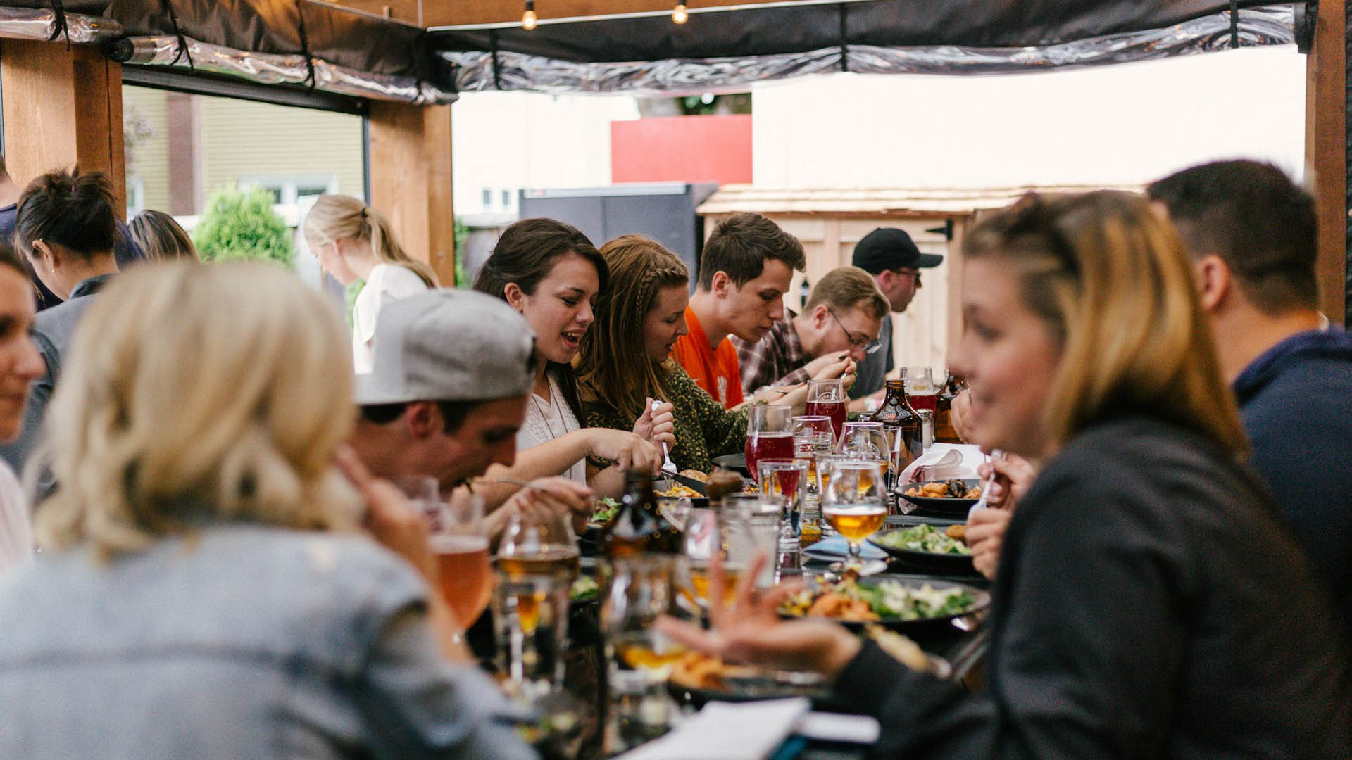 Persone riunite attorno a una lunga tavolata all’aperto che condividono cibo e bevande, simbolo di convivialità durante la Giornata della Ristorazione 2025.