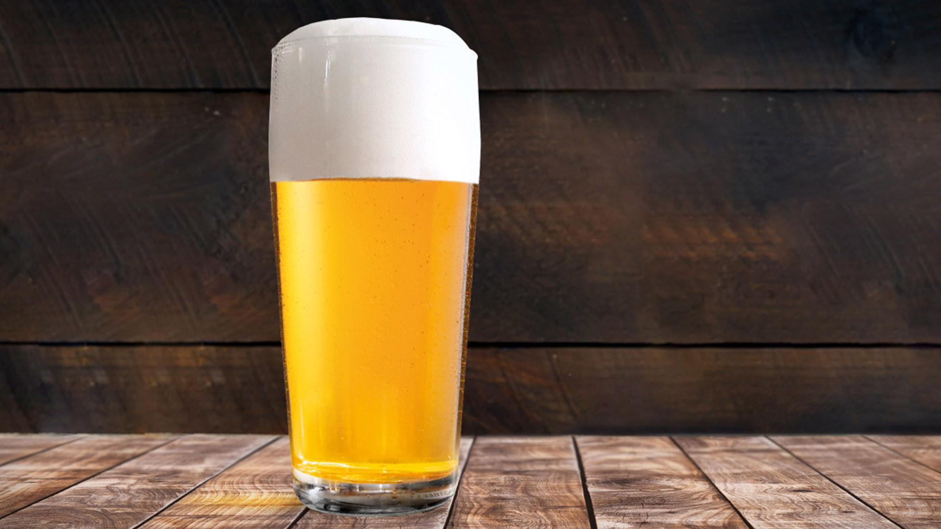 bicchiere di birra pils con schiuma compatta su tavolo in legno, davanti a sfondo rustico in legno scuro