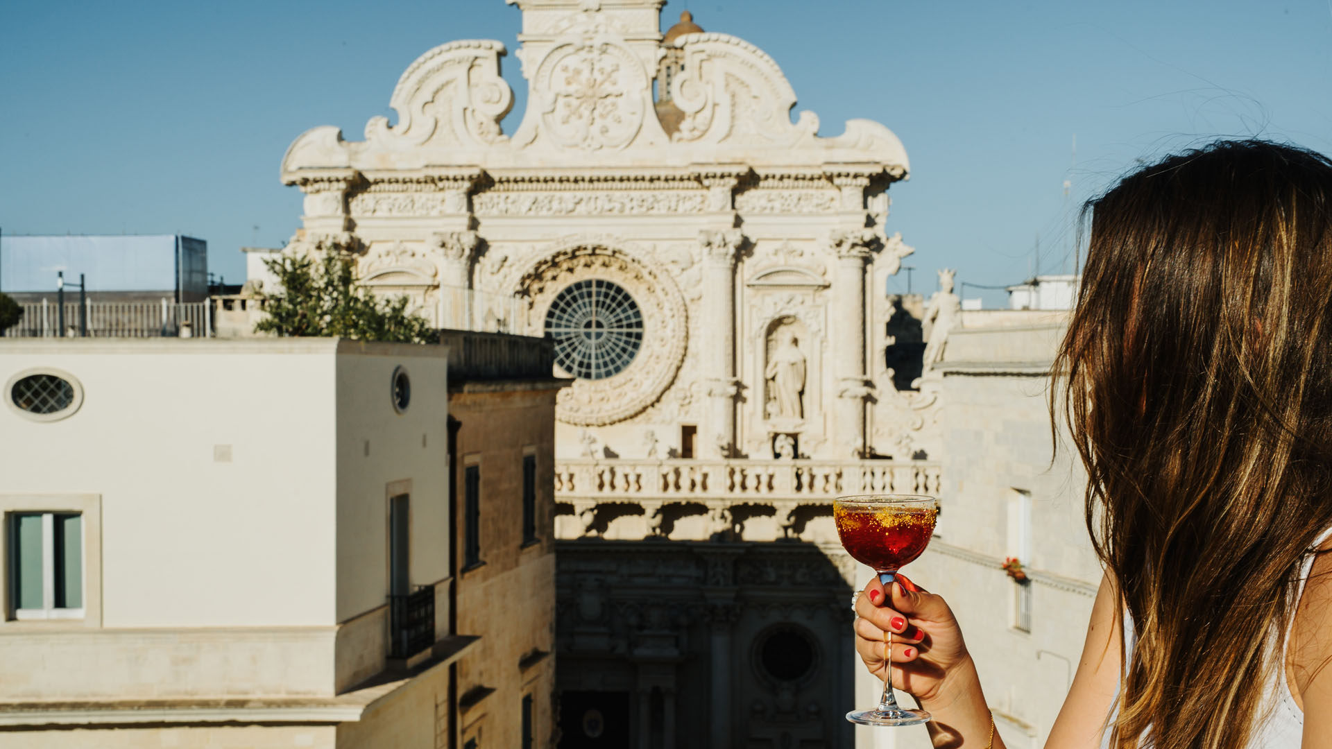 Donna con cocktail a base di rum in mano su terrazza panoramica a Lecce, con vista sulla Basilica di Santa Croce, durante la Lecce Cocktail Week 2025.
