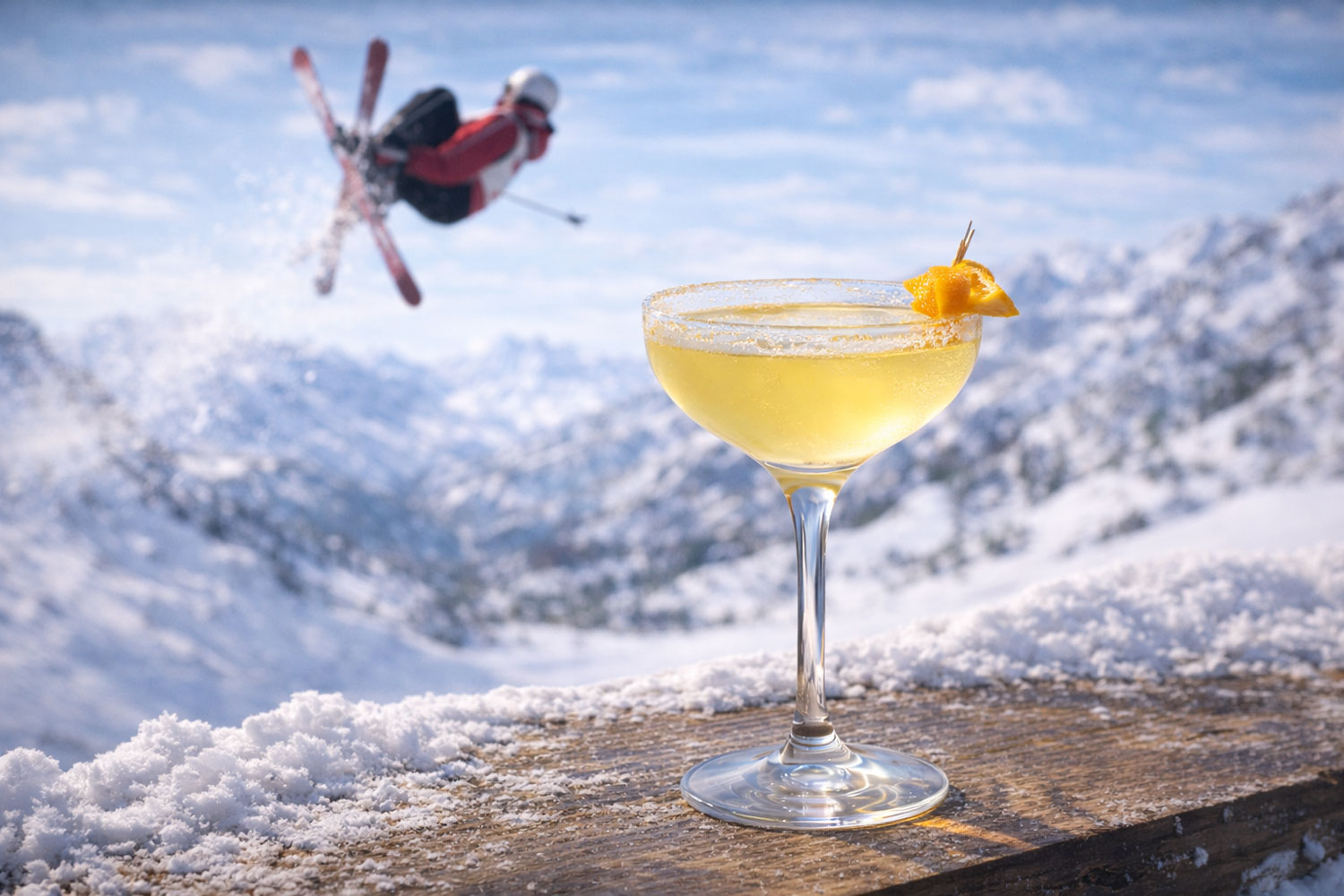 Cocktail Aerial Twist in coppa coupette con garnish agrumato, drink giallo chiaro ispirato al freestyle skiing alle Olimpiadi Invernali 2026, atleta in salto acrobatico sullo sfondo innevato