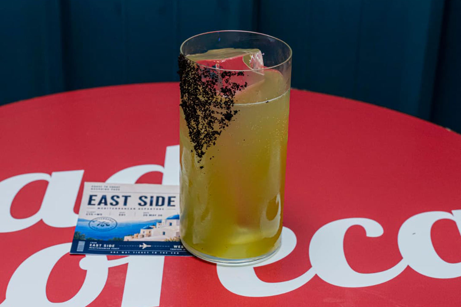 COAST TO COAST – EAST SIDE cocktail di Vito Sciacovelli servito in highball con crusta di olive nere per Raise the Bar 2026.