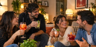 7 cocktail facili da fare a casa, anche senza shaker Quattro amici sorridenti brindano con cocktail preparati in casa, seduti in soggiorno durante un aperitivo