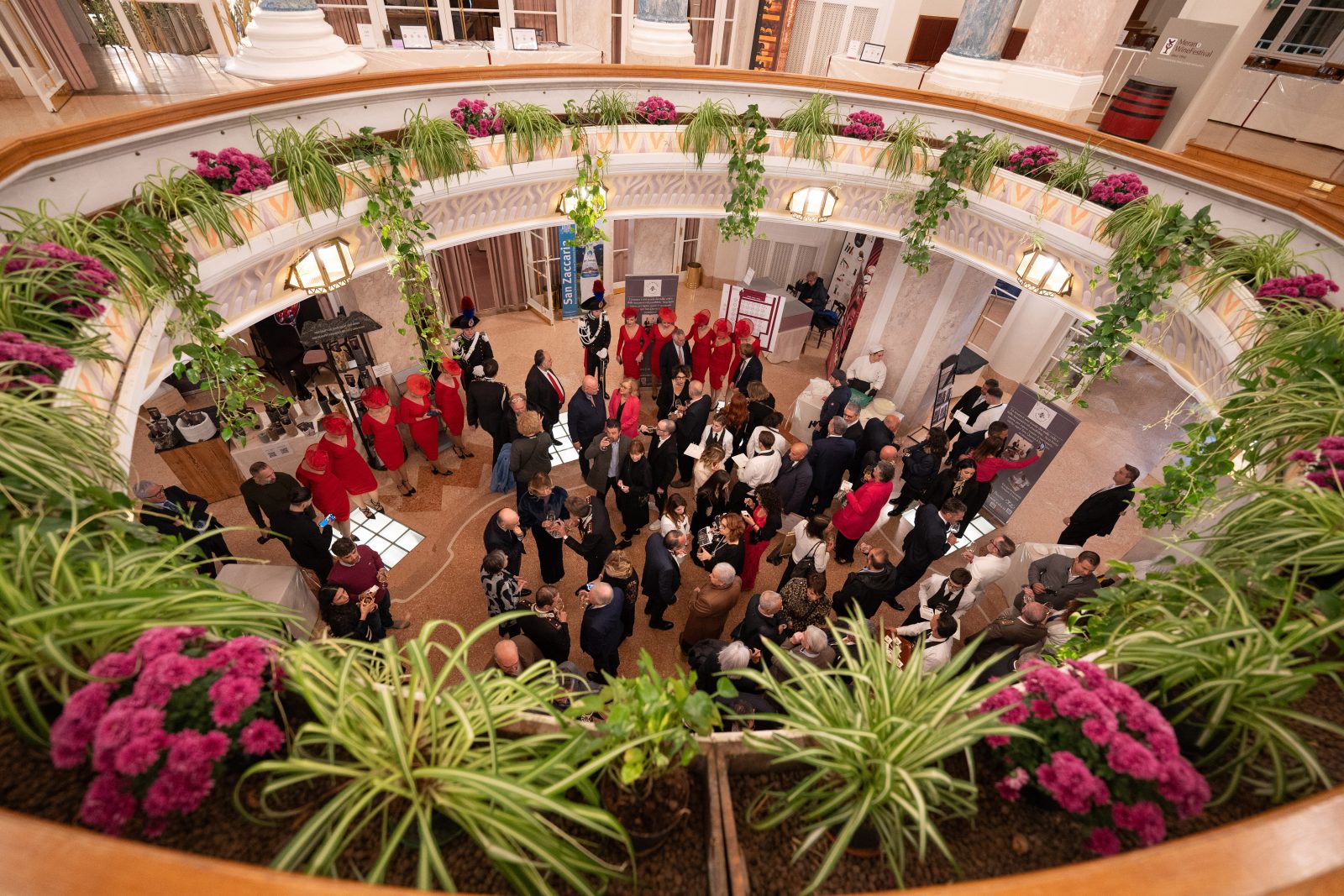 Visitatori e operatori del Merano WineFestival riuniti nell'atrio del Kurhaus, tra allestimenti floreali e spazi espositivi.